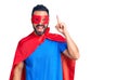Young hispanic man wearing super hero costume pointing finger up with successful idea