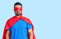 Young hispanic man wearing super hero costume with serious expression on face