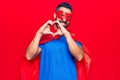 Young hispanic man wearing super hero costume smiling in love doing heart symbol shape with hands Royalty Free Stock Photo