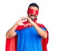 Young hispanic man wearing super hero costume smiling in love showing heart symbol and shape with hands