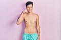 Young hispanic man wearing swimwear shirtless smiling doing phone gesture with hand and fingers like talking on the telephone Royalty Free Stock Photo