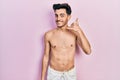 Young hispanic man wearing swimwear shirtless smiling doing phone gesture with hand and fingers like talking on the telephone Royalty Free Stock Photo