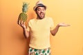 Young hispanic man wearing swimwear and summer hat holding pineapple celebrating achievement with happy smile and winner Royalty Free Stock Photo