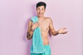 Young hispanic man wearing swimwear and towel celebrating achievement with happy smile and winner expression with raised hand Royalty Free Stock Photo