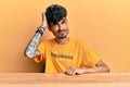 Young hispanic man wearing tshirt with happiness word message sitting on the table confuse and wonder about question