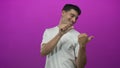 Young hispanic man wearing white tshirt pointing with both thumbs and smiling in purple studio; confidence Royalty Free Stock Photo