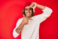 Young hispanic man wearing wool sweater and winter hat smiling making frame with hands and fingers with happy face Royalty Free Stock Photo