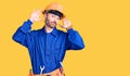 Young hispanic man wearing worker uniform doing bunny ears gesture with hands palms looking cynical and skeptical Royalty Free Stock Photo