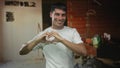 Young hispanic man in white shirt forms heart shape with hands inside building under construction; love joy Royalty Free Stock Photo