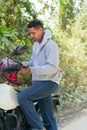 Young Hispanic man in white shirt and jeans putting on helmet near an outdoor motorcycle