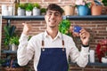 Young hispanic man working at florist shop holding credit card pointing thumb up to the side smiling happy with open mouth Royalty Free Stock Photo