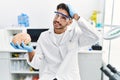 Young hispanic man working at laboratory holding medical brain stressed and frustrated with hand on head, surprised and angry face Royalty Free Stock Photo
