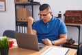 Young hispanic man working at the office with laptop angry and mad raising fist frustrated and furious while shouting with anger Royalty Free Stock Photo