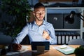 Young hispanic man working at the office at night beckoning come here gesture with hand inviting welcoming happy and smiling Royalty Free Stock Photo