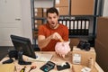 Young hispanic man working at small business ecommerce holding piggy bank in shock face, looking skeptical and sarcastic, Royalty Free Stock Photo