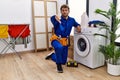 Young hispanic man working on washing machine with angry face, negative sign showing dislike with thumbs down, rejection concept