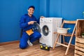 Young hispanic man working on washing machine smiling happy pointing with hand and finger Royalty Free Stock Photo