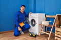 Young hispanic man working on washing machine thinking attitude and sober expression looking self confident Royalty Free Stock Photo