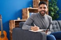 Young hispanic man writing on book sitting on sofa at home Royalty Free Stock Photo