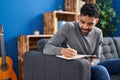 Young hispanic man writing on book sitting on sofa at home Royalty Free Stock Photo