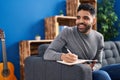 Young hispanic man writing on book sitting on sofa at home Royalty Free Stock Photo