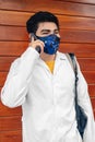 Young Hispanic medical student wearing a facemask and a medical robe and talking on the phone