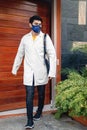 Young Hispanic medical student wearing a facemask and a medical robe while leaving the hospital