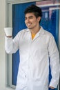 Young Hispanic medical student wearing a medical robe and holding a cup of coffee in a hospital