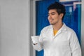 Young Hispanic medical student wearing a medical robe and holding a cup of coffee in a hospital