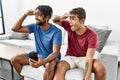 Young hispanic men using smartphone sitting on the sofa at home very happy and smiling looking far away with hand over head Royalty Free Stock Photo