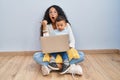 Young hispanic mother and kid using computer laptop sitting on the floor surprised pointing with hand finger to the side, open Royalty Free Stock Photo