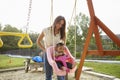 Young Hispanic mother pushing her baby on a swing at a playground in the park Royalty Free Stock Photo