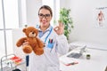 Young hispanic pediatrician woman holding teddy bear at the clinic doing ok sign with fingers, smiling friendly gesturing Royalty Free Stock Photo