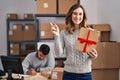 Young hispanic people working at small business ecommerce holding gift smiling happy pointing with hand and finger to the side Royalty Free Stock Photo