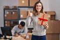 Young hispanic people working at small business ecommerce holding gift smiling happy and positive, thumb up doing excellent and Royalty Free Stock Photo