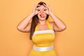 Young hispanic pin up woman wearing fashion sexy 50s style over yellow background doing ok gesture like binoculars sticking tongue Royalty Free Stock Photo