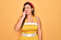 Young hispanic pin up woman wearing fashion sexy 50s style over yellow background looking stressed and nervous with hands on mouth