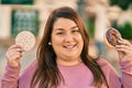 Young hispanic plus size woman smiling happy holding rice cake and donut at the city Royalty Free Stock Photo