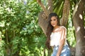 Young, Hispanic, pretty, brunette, young woman in a daisy shirt and jeans, looking at the camera calm and relaxed, leaning against Royalty Free Stock Photo