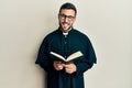 Young hispanic priest man holding bible winking looking at the camera with sexy expression, cheerful and happy face Royalty Free Stock Photo