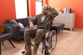 Young hispanic soldier man injured sitting on wheelchair stressed and frustrated with hand on head, surprised and angry face Royalty Free Stock Photo