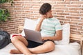 Young hispanic teenager student stressed using laptop sitting on bed at bedroom Royalty Free Stock Photo