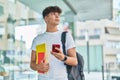 Young hispanic teenager student using smartphone holding books at university Royalty Free Stock Photo