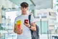 Young hispanic teenager student using smartphone holding books at university Royalty Free Stock Photo