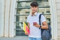 Young hispanic teenager student using smartphone holding books at university Royalty Free Stock Photo