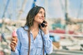 Young hispanic tourist woman talking on the smartphone and eating ice cream at the port Royalty Free Stock Photo
