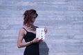 Young Hispanic and transgender girl pointing out in a notebook the letter of her sexual identity, on a gray cement background.