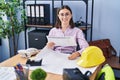 Young hispanic woman architect writing on blueprints reading document at office Royalty Free Stock Photo