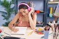 Young hispanic woman artist listening to music drawing on notebook at art studio Royalty Free Stock Photo