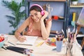 Young hispanic woman artist listening to music drawing on notebook at art studio Royalty Free Stock Photo